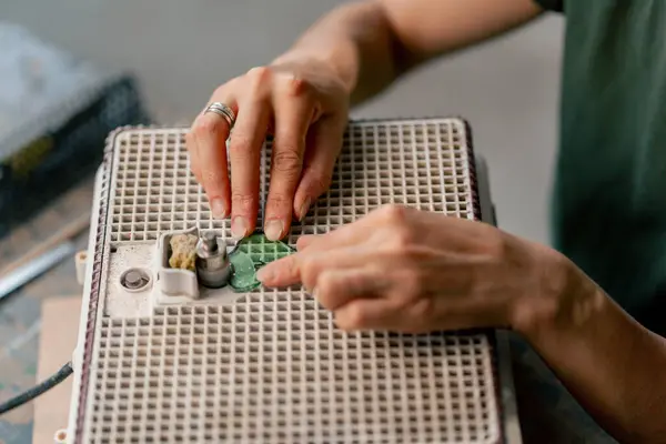 stock image close up in a large green workshop a thin woman with green hair at a wooden table on a grinding machine palates the ends of a glass product, polishing the corners, handmade