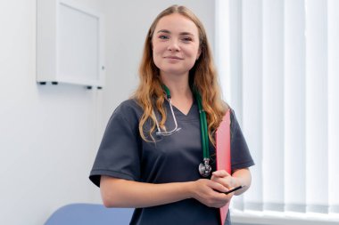 Modern bir klinikte, küçük bir terapistin ofisinde, kırmızı klasör test sonuçlarıyla genç bir doktor, sonuçların değerlendirilmesi, genç ve mutlu bir uzman kameraya bakar.