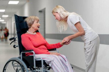 Modern bir klinikte, beyaz bir koridorda, bebek arabasındaki yaşlı bir kadın torununu elinden tutar ve her şeyin yoluna gireceğini söyler, onu sakinleştirir.