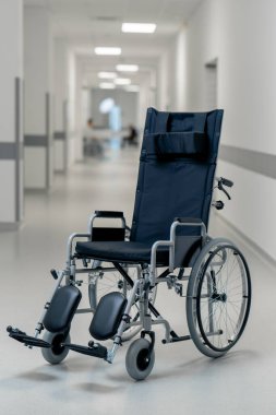 Modern bir klinikte, beyaz bir koridorda engelliler için yeni bir siyah sandalye, hareket yardımı, modern tedavi yöntemleri var.