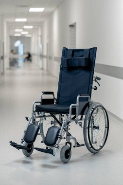 Modern bir klinikte, beyaz bir koridorda engelliler için yeni bir siyah sandalye, hareket yardımı, modern tedavi yöntemleri var.