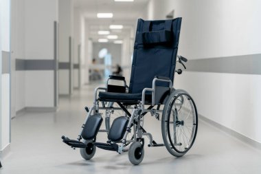 Modern bir klinikte, beyaz bir koridorda engelliler için yeni bir siyah sandalye, hareket yardımı, modern tedavi yöntemleri var.