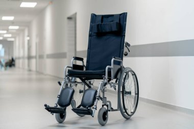 Modern bir klinikte, beyaz bir koridorda engelliler için yeni bir siyah sandalye, hareket yardımı, modern tedavi yöntemleri var.