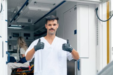 Sokakta bir ambulansta, boynu ve kolu yaralı genç bir hasta bir hastayı kliniğe naklediyor, genç bir doktor da arabanın önünde.