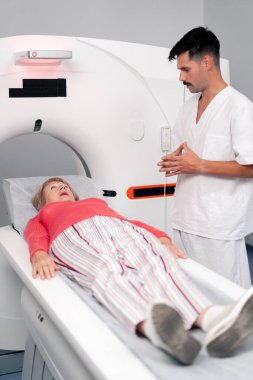 Modern bir klinikte, beyaz bir ofiste yaşlı bir kadının, yakınlardaki genç bir doktorun beyin MR 'ı için bir ilaç.