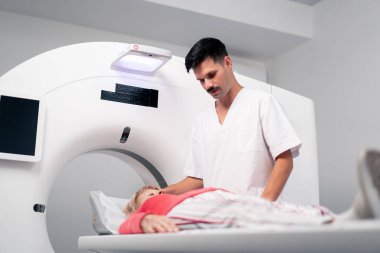 Modern bir klinikte, beyaz bir ofiste yaşlı bir kadının, yakınlardaki genç bir doktorun beyin MR 'ı için bir ilaç.