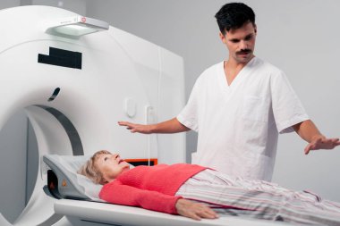 Modern bir klinikte, beyaz bir ofiste yaşlı bir kadının, yakınlardaki genç bir doktorun beyin MR 'ı için bir ilaç.