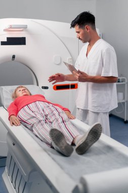 Modern bir klinikte, beyaz bir ofiste yaşlı bir kadının, yakınlardaki genç bir doktorun beyin MR 'ı için bir ilaç.