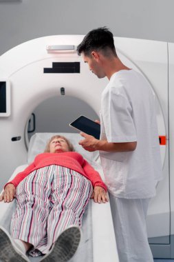 Modern bir klinikte, beyaz bir ofiste yaşlı bir kadının, yakınlardaki genç bir doktorun beyin MR 'ı için bir ilaç.