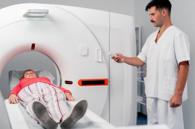 Modern bir klinikte, beyaz bir ofiste yaşlı bir kadının, yakınlardaki genç bir doktorun beyin MR 'ı için bir ilaç.