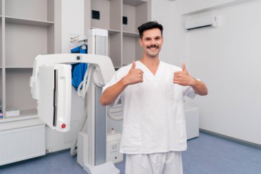 Modern bir klinikte, beyaz bir ofiste, florografi görüntüleri için bir hazırlık, hastaların güvenli bir şekilde incelenmesi için son teknolojiler, beyaz üniformalı, gülümseyen genç bir doktor,