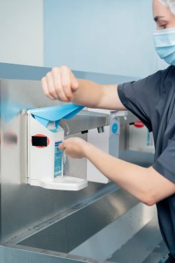 Cerrahların ellerini sterilize etmek için geniş bir alanda modern klinikte kapatılan kadın cerrah ellerini iyice yıkıyor.