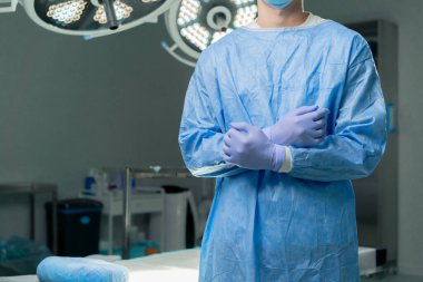 Modern bir klinikte, parlak, geniş bir ameliyathanede cerrah ameliyatı yapmak için tamamen hazırdır.