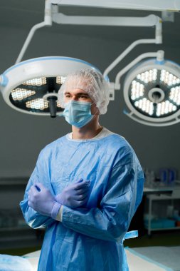 Modern bir klinikte, parlak, geniş bir ameliyathanede cerrah ameliyatı yapmak için tamamen hazırdır.