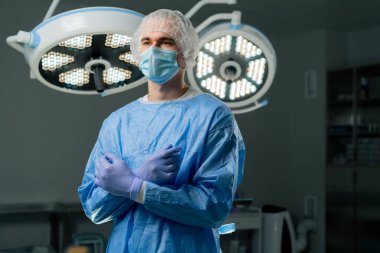 Modern bir klinikte, parlak, geniş bir ameliyathanede cerrah ameliyatı yapmak için tamamen hazırdır.