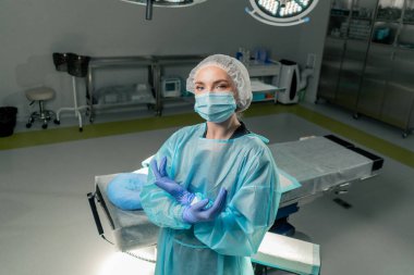 Modern bir klinikte, parlak, geniş bir ameliyathanede cerrah ameliyatı yapmak için tamamen hazırdır.