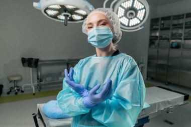 Modern bir klinikte, parlak, geniş bir ameliyathanede cerrah ameliyatı yapmak için tamamen hazırdır.