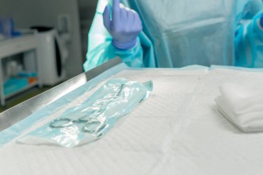 Modern klinikte, parlak, geniş bir ameliyathanede steril eldivenli bir doktor paketleri açmak için cerrahi klemp alır ve...