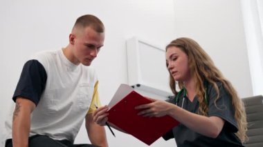 Modern klinikte, küçük bir terapistin ofisinde, steteskoplu genç bir doktor test sonuçları olan genç bir hastayı muayene ediyor.