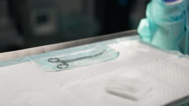 Modern klinikte, parlak, geniş bir ameliyathanede steril eldivenli bir doktor paketleri açmak için cerrahi klemp alır ve...