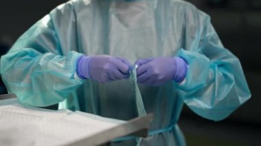 Modern klinikte, parlak, geniş bir ameliyathanede steril eldivenli bir doktor paketleri açmak için cerrahi klemp alır ve...