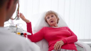 Modern bir klinikte, beyaz bir ofiste, kalp ritmini ölçmek için bir ilaç, bir kardiyogram, bir doktor hastanın şikayetlerini dinler.