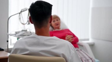Modern bir klinikte, beyaz bir ofiste, kalp ritmini ölçmek için bir ilaç, bir kardiyogram, bir doktor hastanın şikayetlerini dinler.