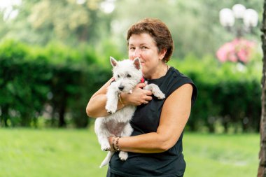 Yazın parkta yürürken koyu saçlı bir kadın kollarında bir Maltese köpeği taşır. Hayvanlara olan sevgisi sahibinin parkında yürür.