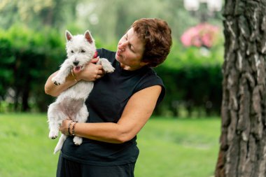 Yazın parkta yürürken koyu saçlı bir kadın kollarında bir Maltese köpeği taşır. Hayvanlara olan sevgisi sahibinin parkında yürür.