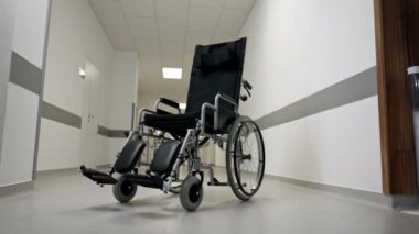 Modern bir klinikte, beyaz bir koridorda engelliler için yeni bir siyah sandalye, hareket yardımı, modern tedavi yöntemleri var.