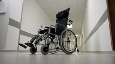 Modern bir klinikte, beyaz bir koridorda engelliler için yeni bir siyah sandalye, hareket yardımı, modern tedavi yöntemleri var.