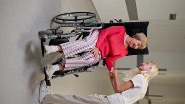 Modern bir klinikte beyaz bir koridorda dikey bir video, bebek arabasındaki yaşlı bir kadın torununu elinden tutar ve her şeyin yoluna gireceğini söyler, onu sakinleştirir.