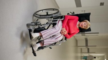 Modern bir klinikte beyaz bir koridorda dikey bir video, bebek arabasındaki yaşlı bir kadın torununu elinden tutar ve her şeyin yoluna gireceğini söyler, onu sakinleştirir.