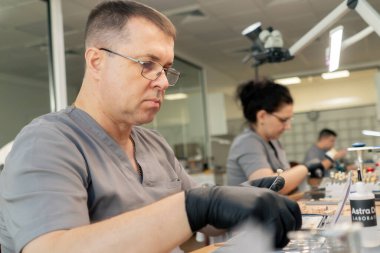 Diş protozoası ve taç kaplaması üretimi için profesyonel bir laboratuvar. Müşterinin dişlerinin altında diş fırçası ve diş minesi kaplaması olan bir boya uzmanı oturuyor.