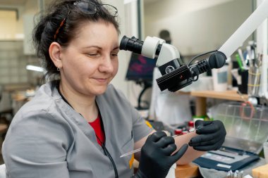 Diş protezleri üretimi için profesyonel laboratuvar kadın kaplama uzmanı kameraya bakarak büyüteç kullanarak diş şeklini yeniden yaratıyor.