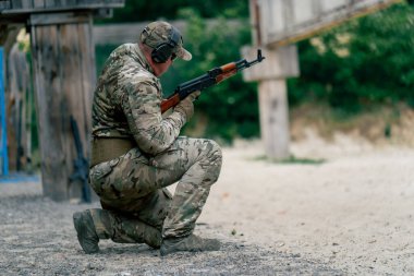 Askeri strateji tüfeği pozisyonu. Askeri üniformalı bir atış poligonu eğitmeni için eğitim pozisyonu. Başka bir askere dizinden vurulması için işaret veriyor.