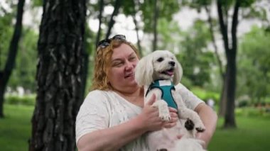 Yazın parkta yürürken şişman yaşlı bir kadın, hayvanlara olan sevgisiyle Maltalı bir köpeği kucağına alır. Parkta sahibinin bakımıyla yürür.