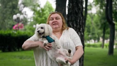 Yazın parkta yürürken şişman yaşlı bir kadın kollarında bir Maltese köpeği taşır hayvanlara olan sevgisi sahibinin parkında yürür.