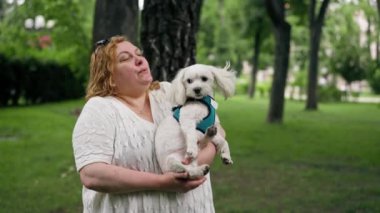 Yazın parkta yürürken şişman yaşlı bir kadın kollarında bir Maltese köpeği taşır hayvanlara olan sevgisi sahibinin parkında yürür.