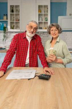 Parlak bir mutfakta, masadaki yaşlı, sevimli bir çift aylık ödeme faturalarını sayıyor aylık hayatta kalma masrafları kameraya bakıp gülümsüyor.