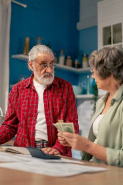 Aydınlık bir mutfakta, masadaki yaşlı bir çift aylık giderlerini hesaplar. Yıllık giderlerini hesaplarlar. Aylık yaşam süresini sayarlar.
