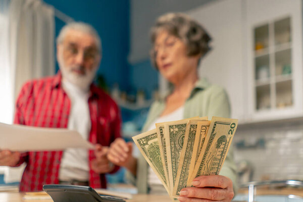close up money in a bright kitchen an elderly cute couple at the table count their expenses monthly payment summing up the results of the year utilities count monthly survival count money