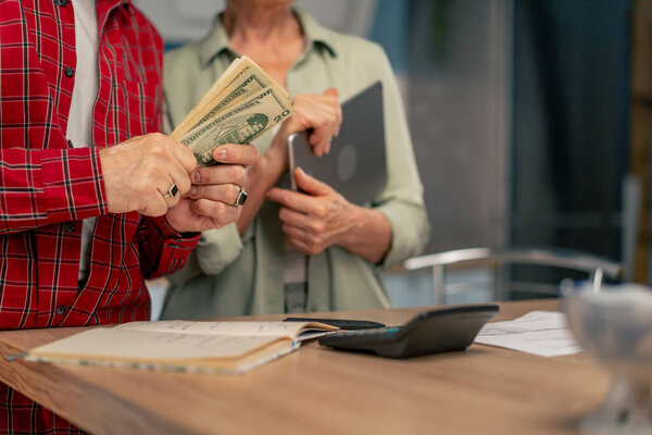 close-up in a bright kitchen hands with American bills calculator payment receipts calculator hard pension utilities