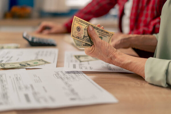 close-up in a bright kitchen hands with American bills calculator payment receipts calculator hard pension utilities