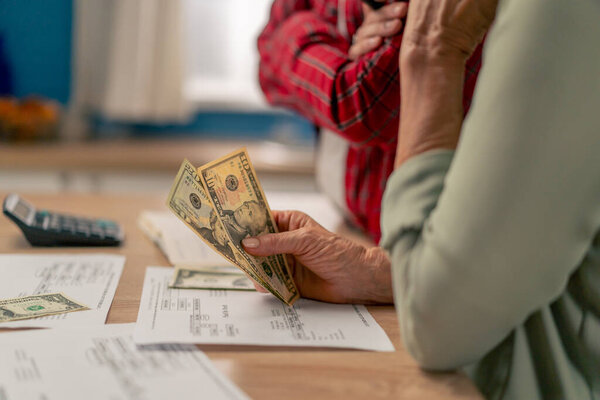 close-up in a bright kitchen hands with American bills calculator payment receipts calculator hard pension utilities