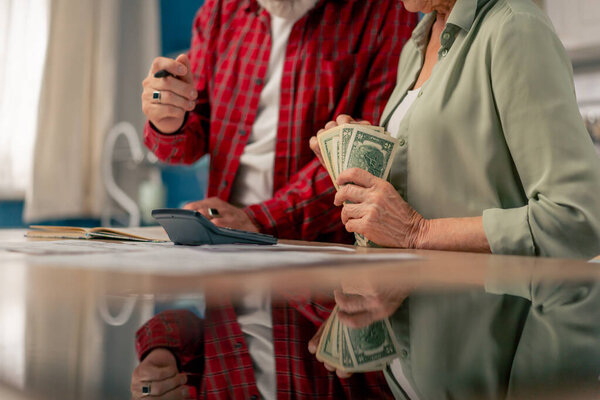 close-up in a bright kitchen hands with American bills calculator payment receipts calculator hard pension utilities