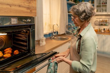 Parlak bir mutfakta açık yeşil tişörtlü yaşlı bir kadın fırından taze turtalar çıkarıyor. Mutfakta mutlu, yaşlı bir ev hanımı.