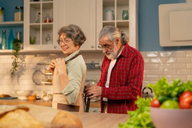 Parlak bir mutfakta kırmızı gömlekli yaşlı bir adam yemek yapmadan önce arkasından gülümsüyor. Karısı için önlük bağlıyor. Mutlu bir çift.