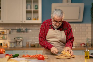 Mutfakta, ahşap bir masanın üstünde önlüklü yaşlı bir adam yaşlı insanların hayatlarını kesiyor.