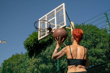 Kısa şortlu, siyah tişörtlü, kısa saçlı, spor sahasındaki aktif eğlence kızı çeviklik antrenmanına basketbol topu atmak için yakın çekim.